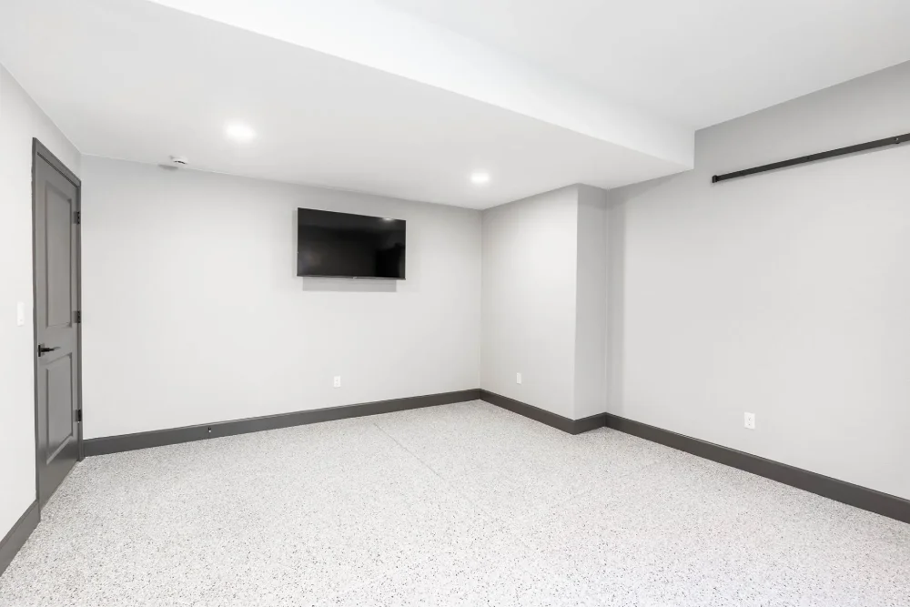 Finished 300-square-foot basement gym and workshop with speckled epoxy flooring, wall-mounted TV, and a dark gray paneled door