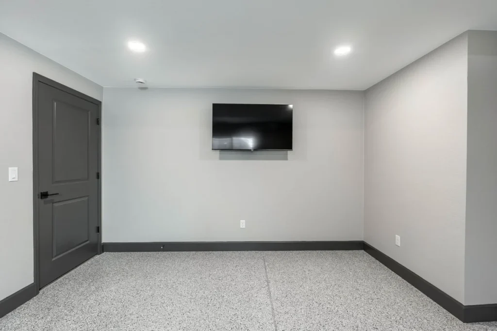Finished basement wall with mounted TV and dark grey door in a home gym remodel in Littleton, CO.
