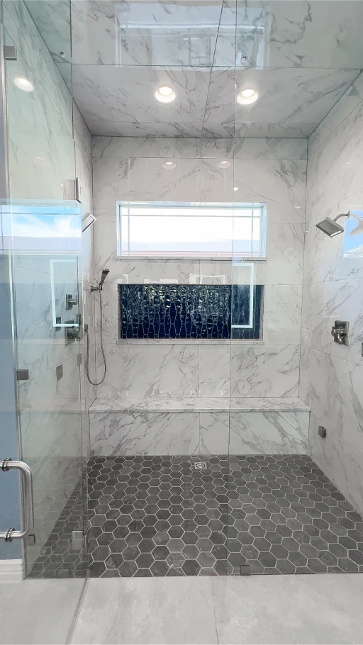 Aurora, CO walk-in shower conversion with marble-look walls, glass enclosure, hexagon floor tile, bench, blue tiled niche, and dual shower heads.