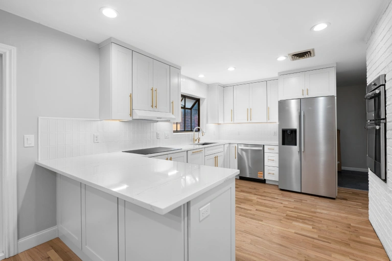 Renovated kitchen with white shaker cabinets, gold hardware, quarts countertop and backsplash, and hardwood flooring completed at S. Josephine St, Denver, CO 80210 by Verified Builders kitchen remodel contractors