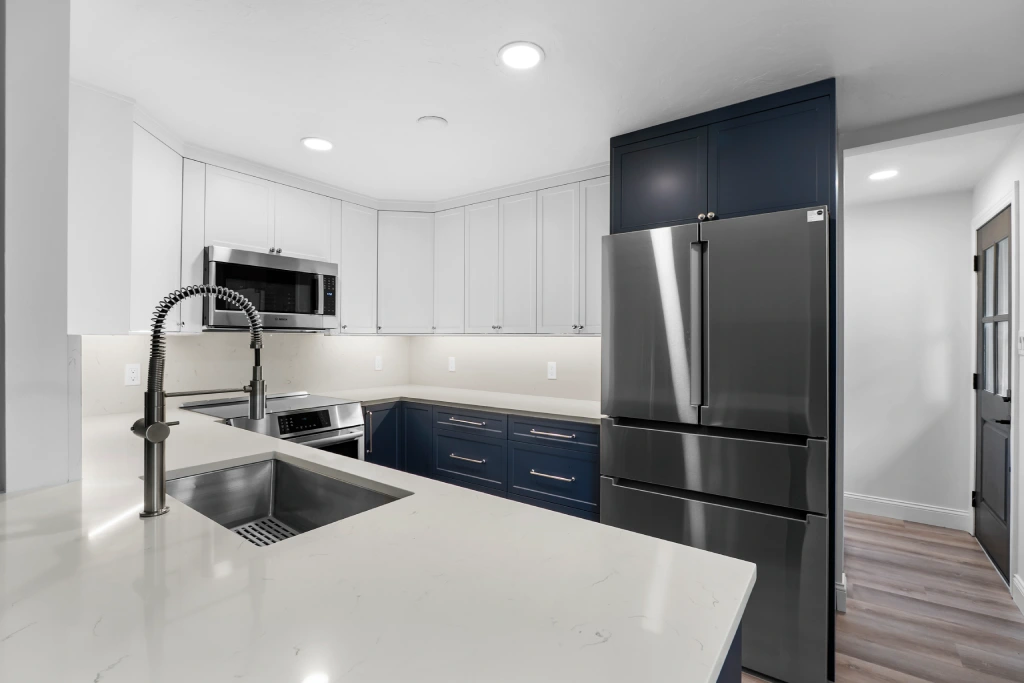 After kitchen remodel on W 107th Ave in Westminster, CO 80021 featuring two-tone white and navy shaker cabinets, quartz countertops, stainless appliances, and modern pull-down faucet.