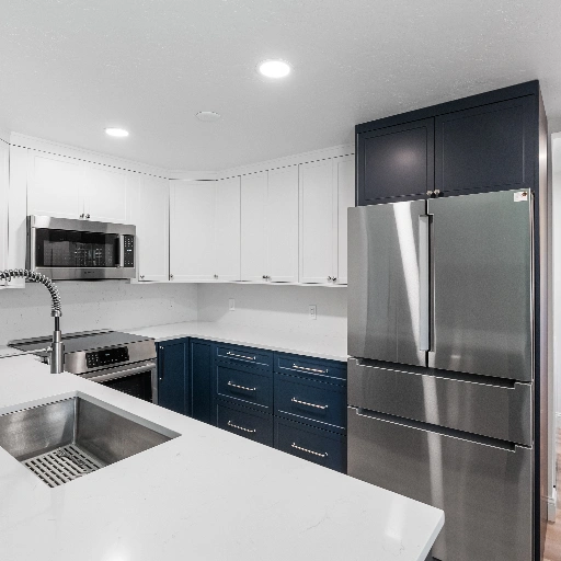 Modern Westminster kitchen remodel featuring semi-custom white upper cabinets, navy blue base cabinets, stainless steel appliances, white quartz countertops, and a deep undermount sink by Verified Builders.