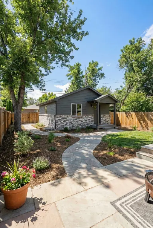 A modern detached ADU with stamped concrete patio in a backyard at 5000 W 17th Ave, Denver. The standalone structure serves as a private guest suite or rental unit, featuring gray fiber cement siding and brick accents.