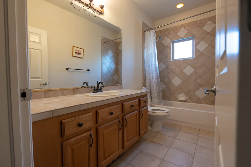 "Before" guest bath vanity with oak cabinetry and tile countertops on Hawks Nest Trail, Littleton, before a modern upgrade.