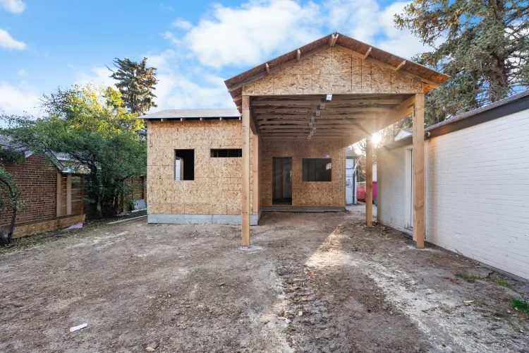 Exterior construction view of a 150 sq ft covered patio addition in Denver, featuring engineered roof trusses and OSB sheathing ready for weatherproofing and shingle roofing.