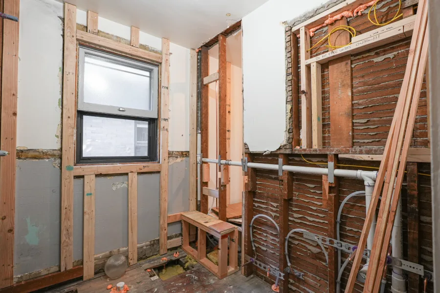 The "before" state of a hallway bathroom remodel in Denver, CO 80206, showing the original tub area stripped to the wood framing before its conversion into a modern walk-in shower.