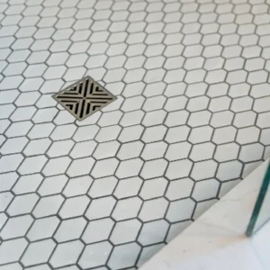 Slip-resistant white hexagon mosaic shower floor tile with dark grout in a Littleton, Colorado master bathroom renovation, featuring a square chrome drain.