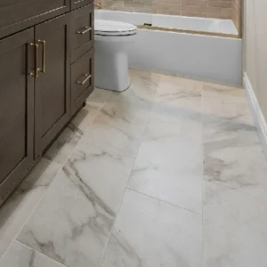 Hallway bathroom remodel in Littleton, Colorado, featuring durable large-format porcelain tile flooring, a dark wood vanity with gold hardware, and a tub shower combo with beige subway tile.
