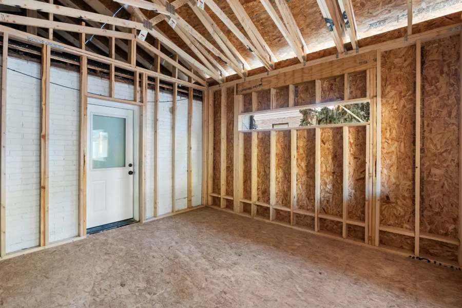 Interior framing stage of a 425 sq ft primary suite addition on Holly St, Denver, showing exposed studs, vaulted ceiling structure, and window rough opening.