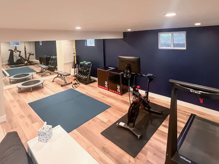 Finished basement home gym in the Denver metro area featuring LVP flooring, recessed lighting, and a mirrored wall, completed by Verified Builders.