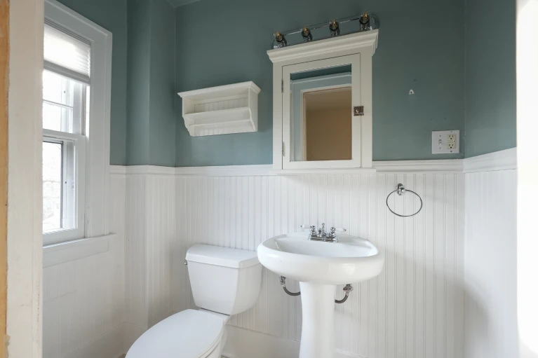 Existing powder room with medicine cabinet and chrome sconce before the full bath conversion.