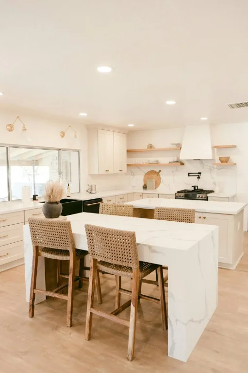 Remodeled Centennial kitchen by Verified Builders with a waterfall marble island, woven counter stools, light wood cabinetry, and oak flooring