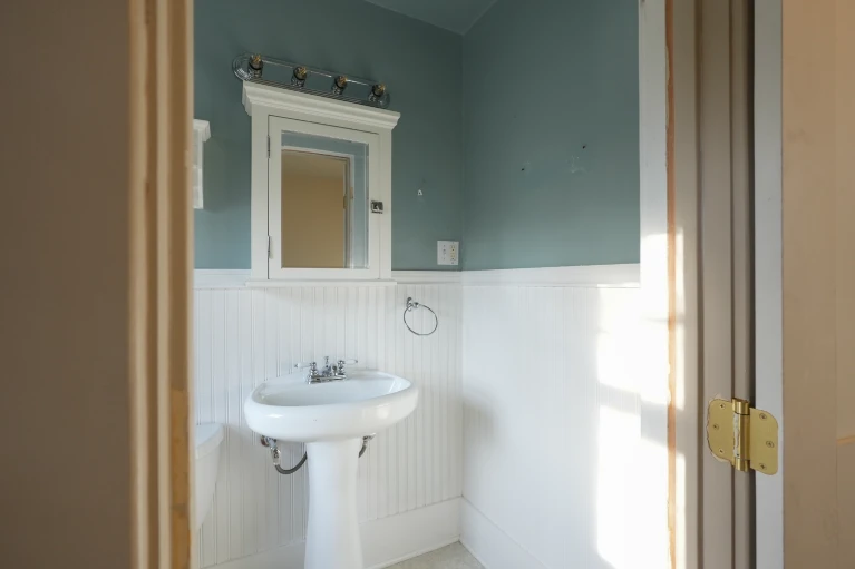 West Highland Denver powder room before remodel, with pedestal sink, mirror, and chrome vanity light.