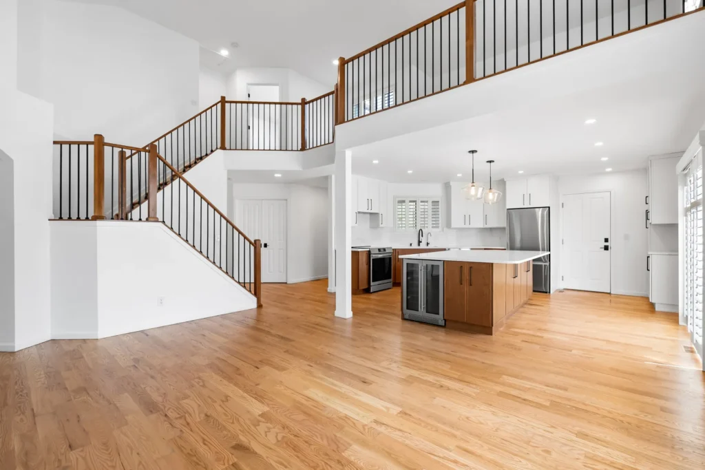 Open-concept kitchen and living space after a whole house remodel in Arvada, CO, with refinished oak hardwood floors, a two-tone island kitchen, and a new staircase railing
