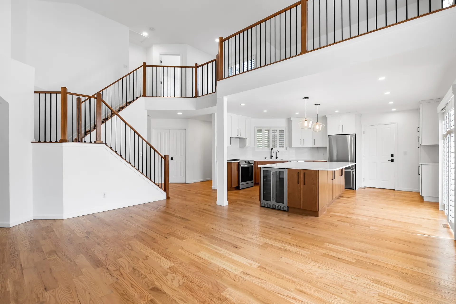Open-concept kitchen and living space after a whole house remodel in Arvada, CO, with refinished oak hardwood floors, a two-tone island kitchen, and a new staircase railing