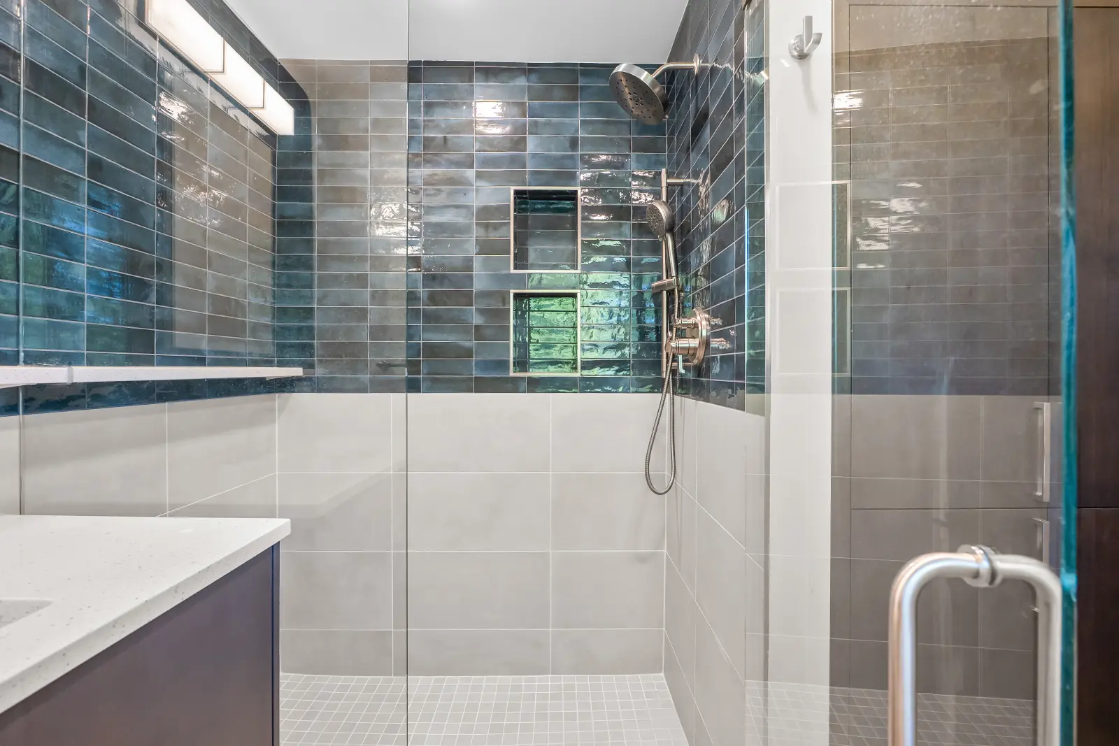 Interior of curbless walk-in shower with blue Mir Moda tile, Fab Crete mosaic floor, and Kohler fixtures in Park Hill Denver