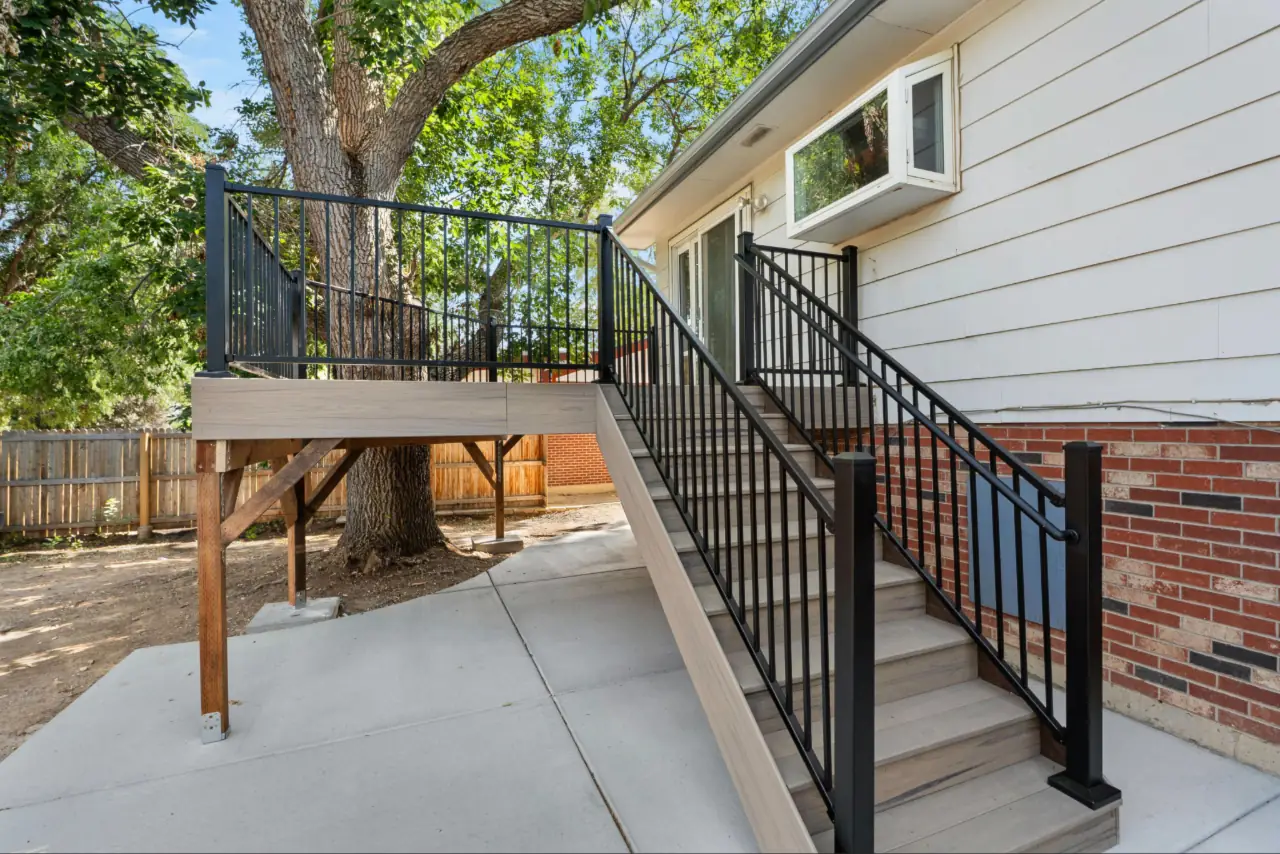 Finished Trex composite deck with black aluminum railings and rebuilt stairs at a Northglenn Colorado home, wrapped around a mature backyard tree